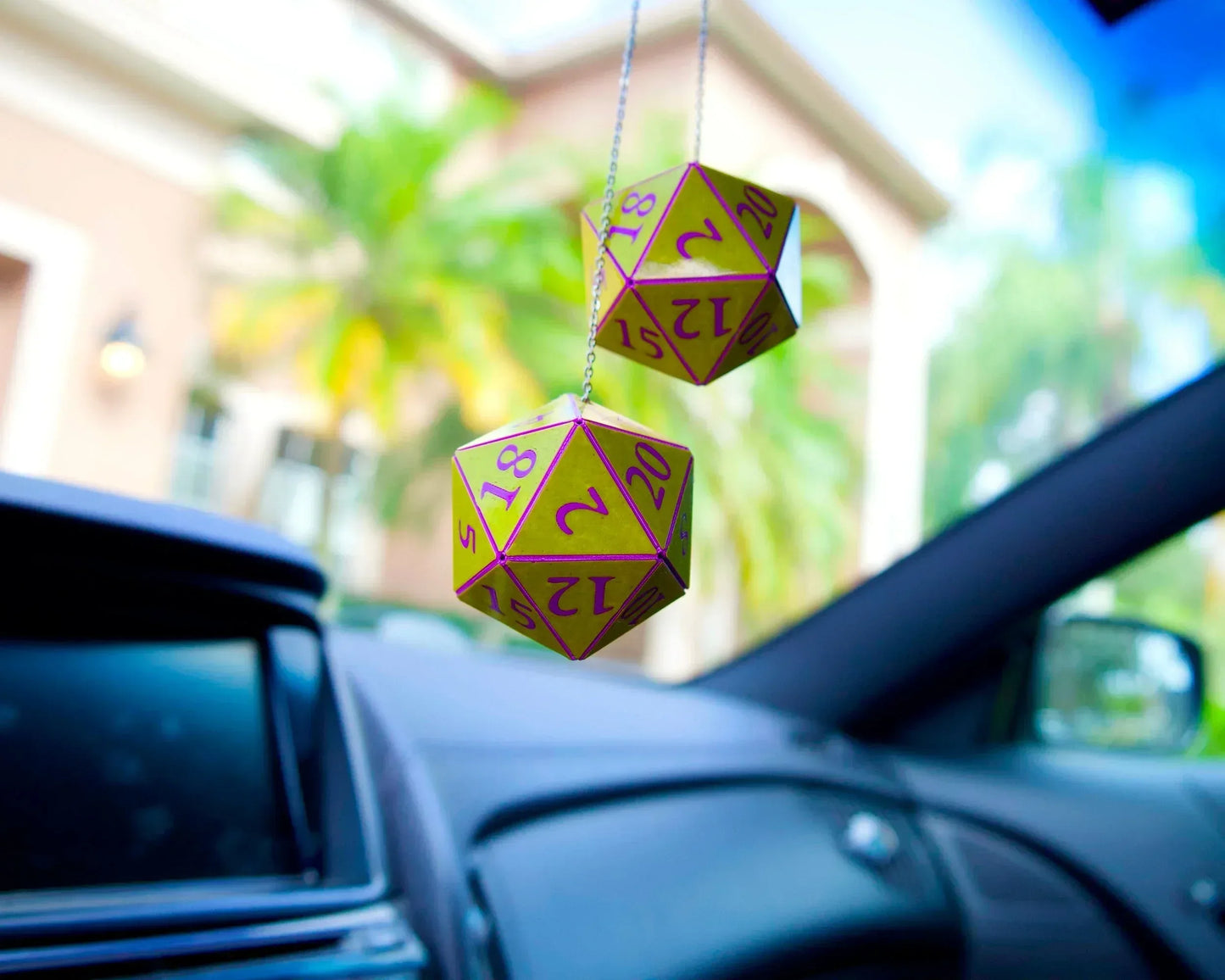 Holographic twenty-sided dice car charm hanging from rearview mirror in a car interior.