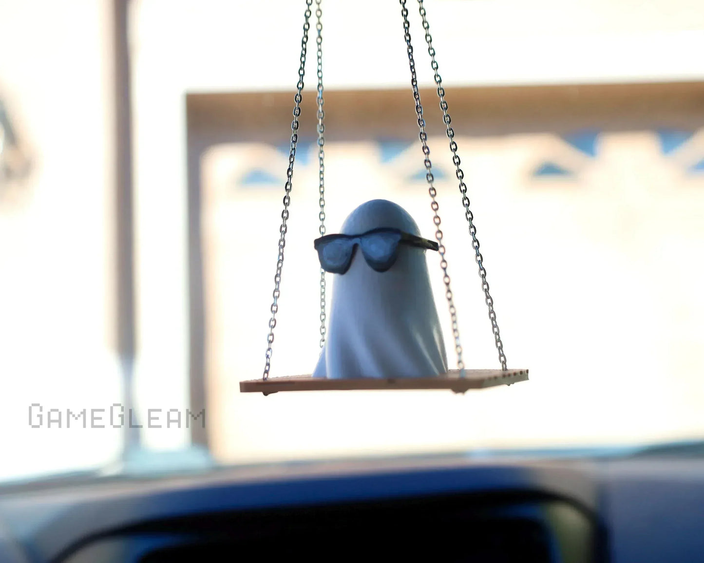 Handmade ghost car charm with sunglasses on a swing, hanging in a vehicle interior
