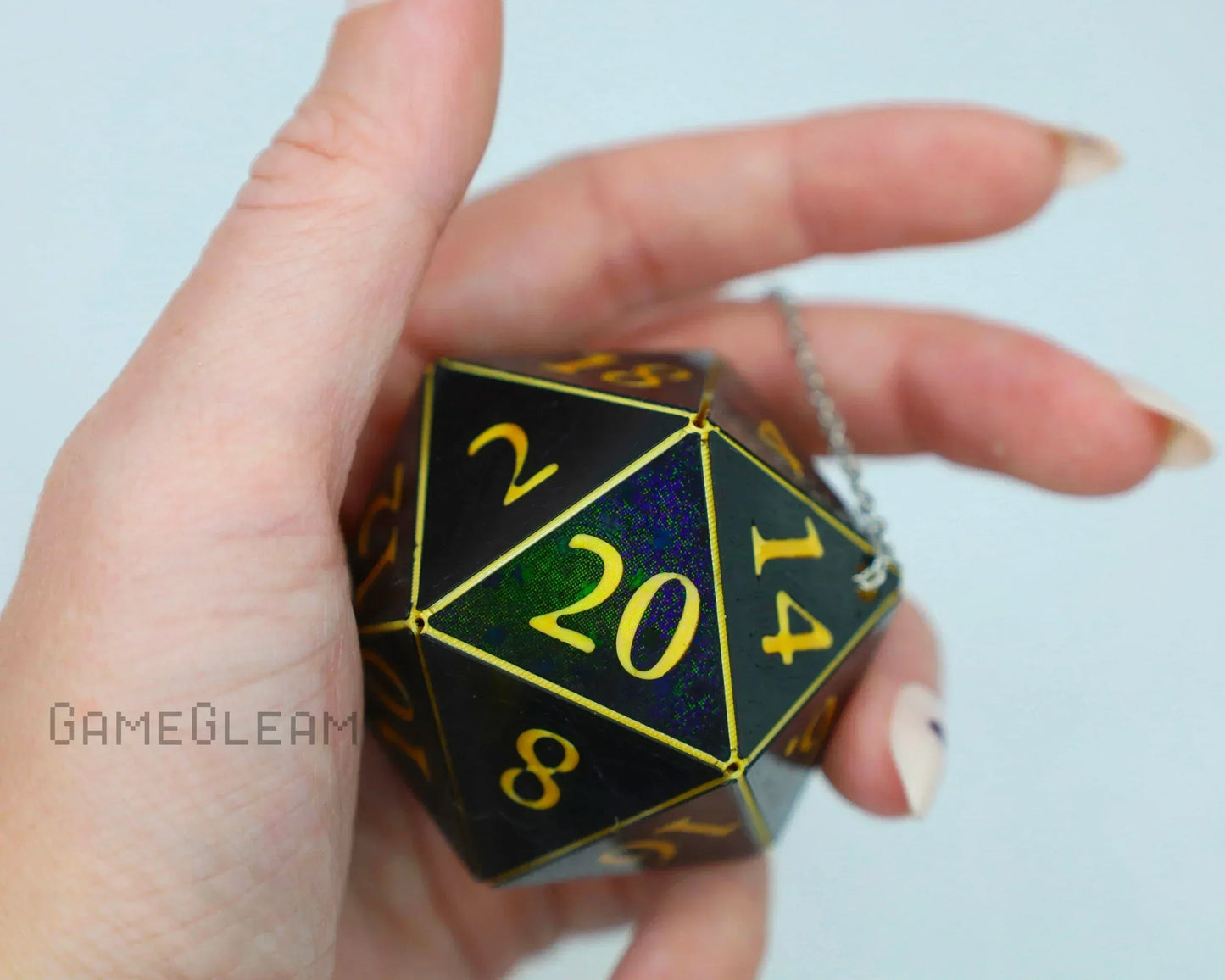 Hand holding holographic black and gold twenty-sided dice keychain for tabletop games