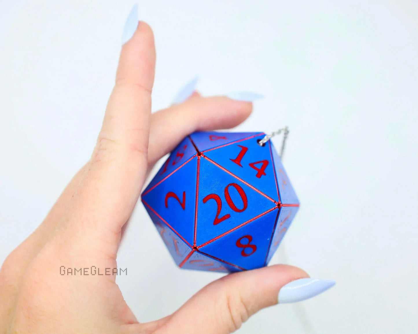 Blue twenty-sided dice car charm with red numbers held by a hand, silver chain attached