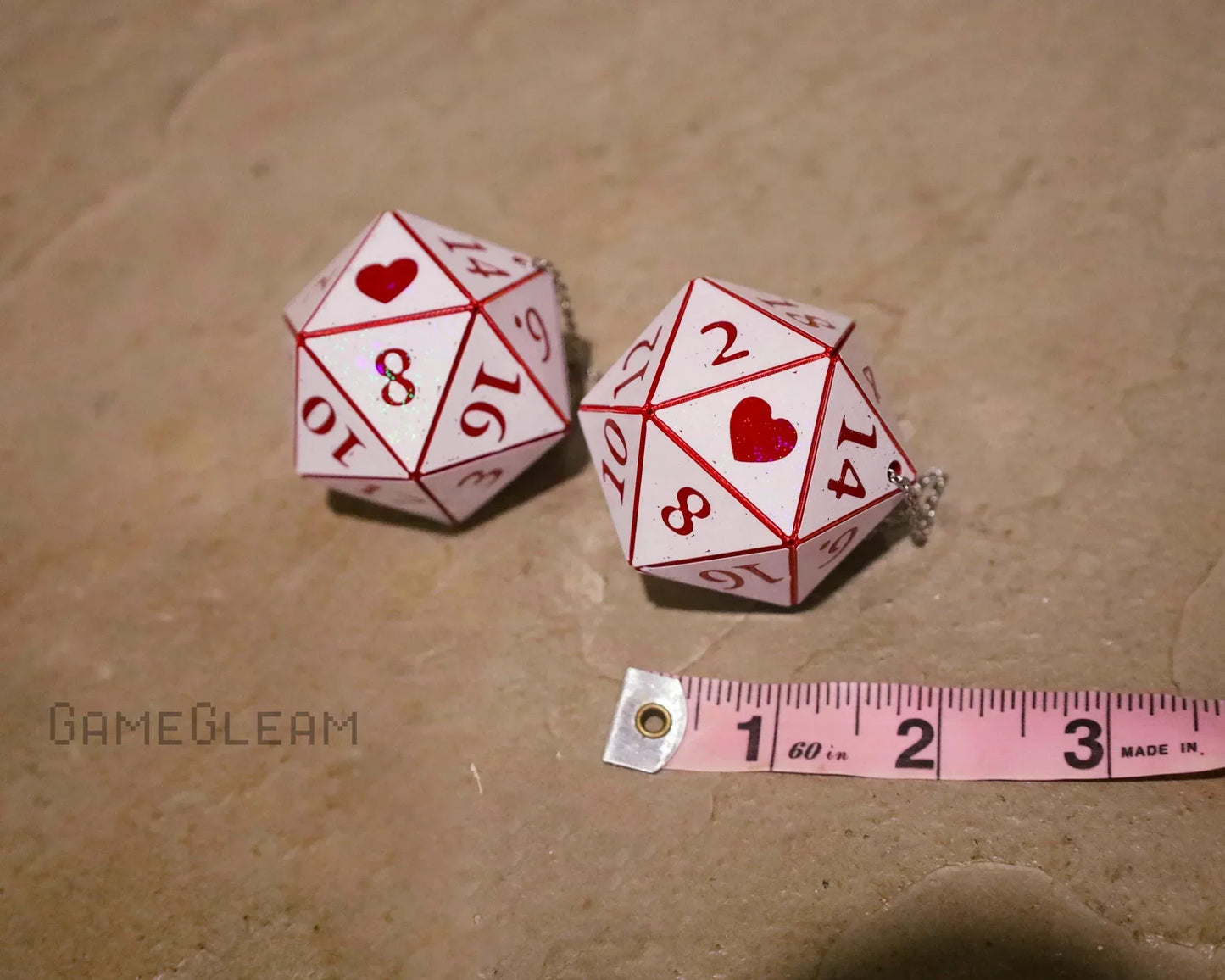 Pair of white 20-sided dice with red hearts and numbers, shown with a measuring tape