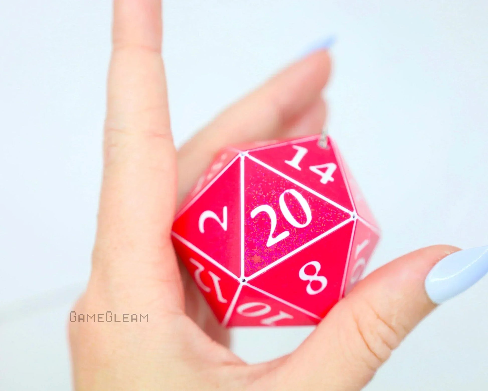 Hand holding a large pink 20-sided dice charm with white numbers, ideal for tabletop gaming fans.