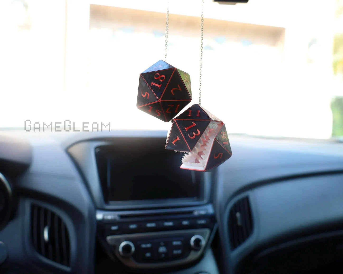 Hanging car charm with two black and red polyhedral dice, one with monster teeth, inside a vehicle.
