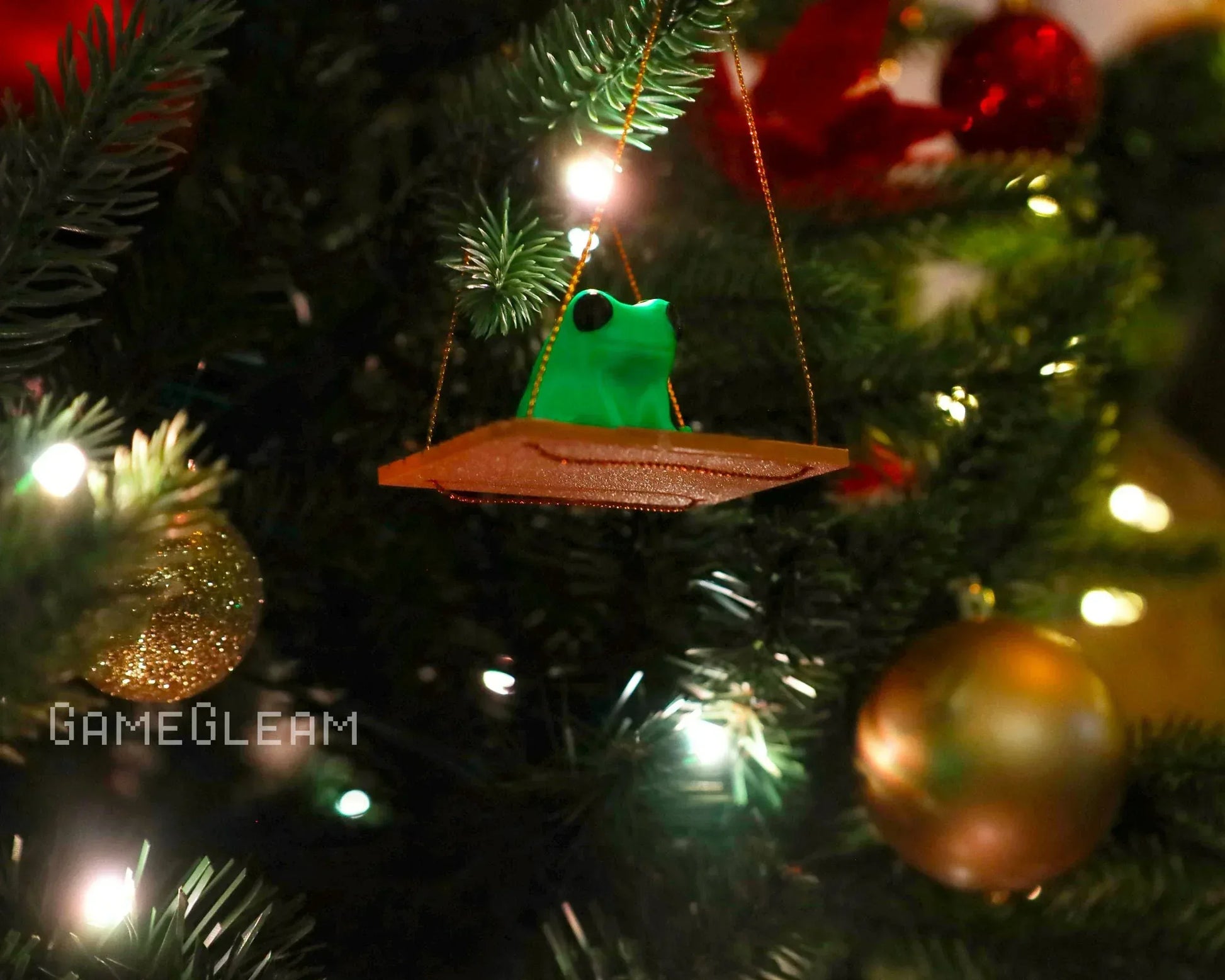 Handmade frog ornament on swing hanging from Christmas tree with festive lights and baubles