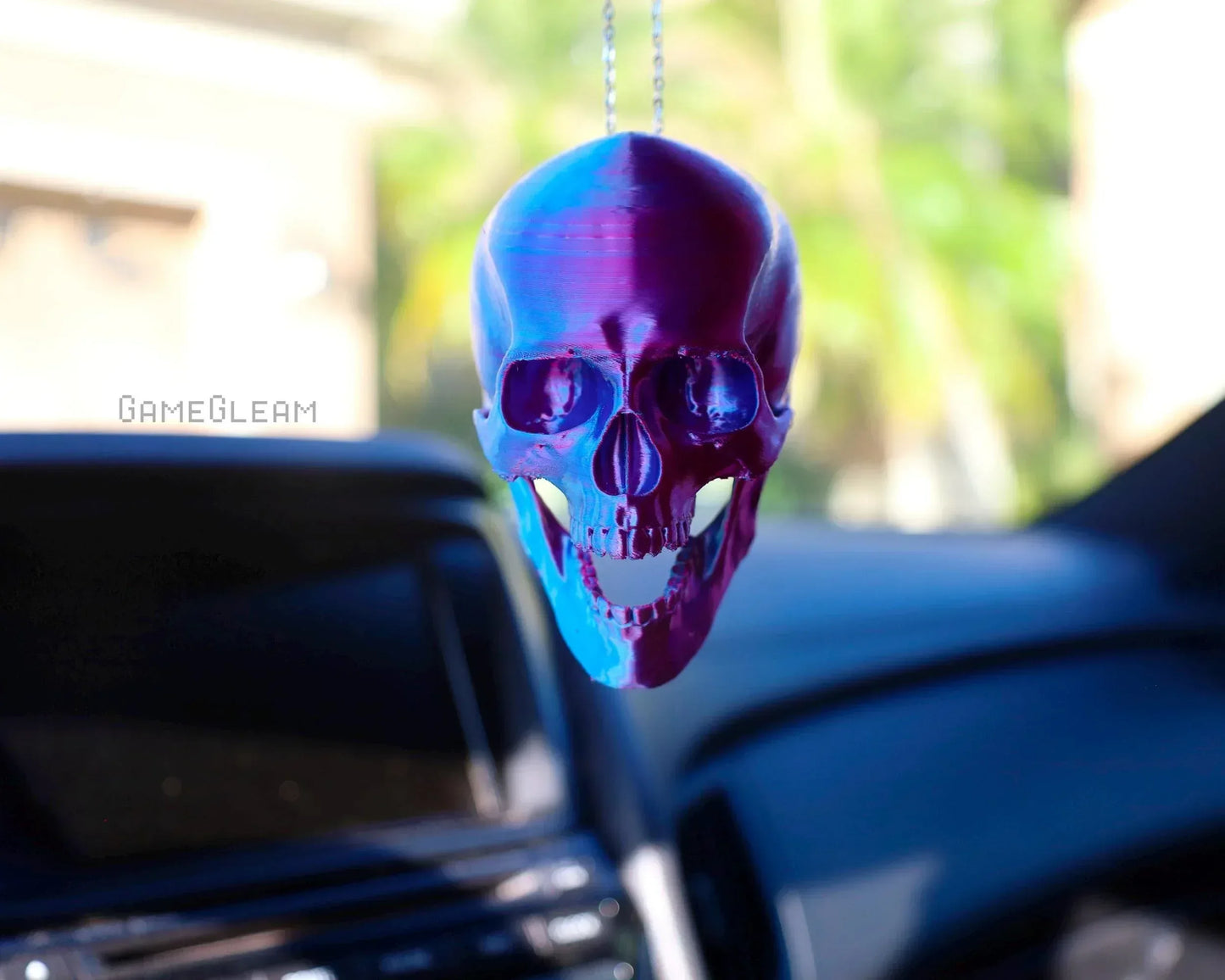 Holographic purple and blue skull car charm hanging from a rearview mirror in a car interior.