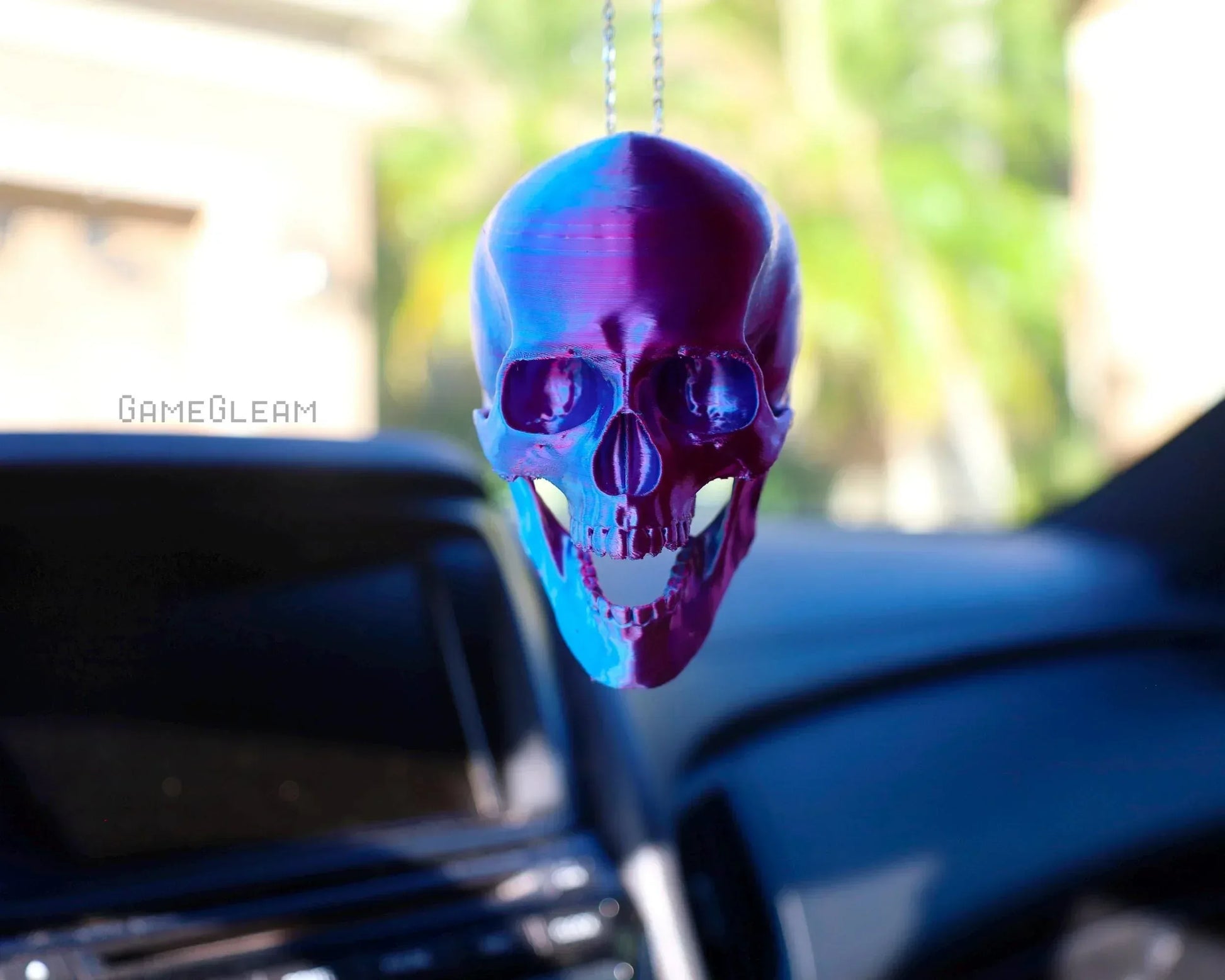 Holographic purple and blue skull car charm hanging from a rearview mirror in a car interior.