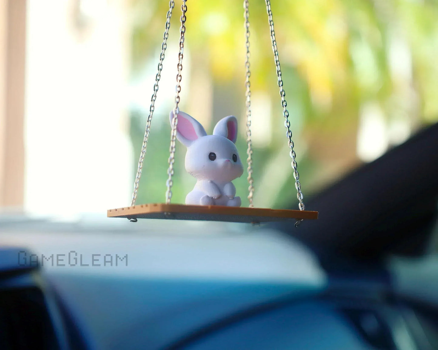 Cute bunny figurine car charm on a swinging platform, hanging by chains, in a vehicle.