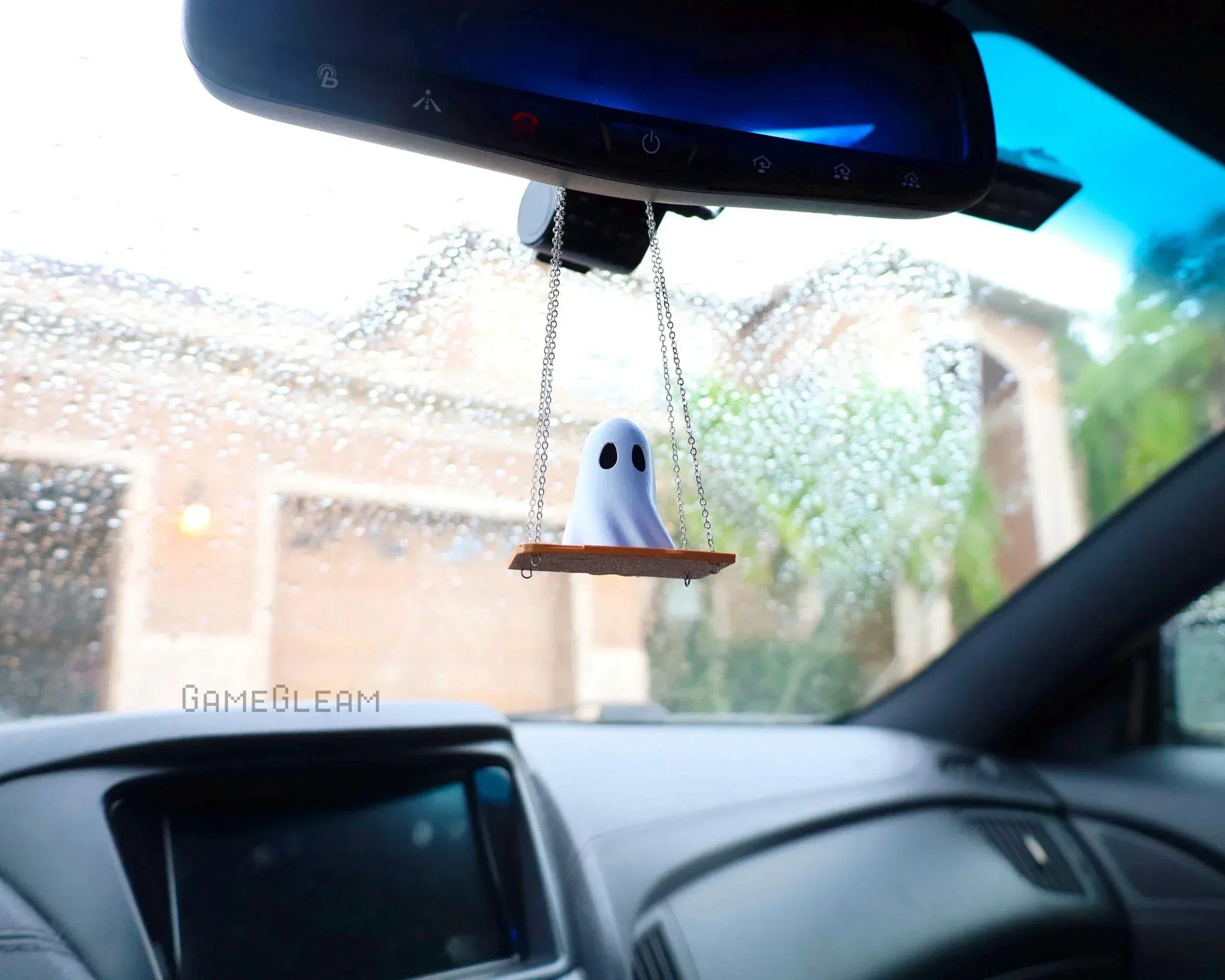 Handmade ghost car charm on swing hanging from rearview mirror inside car on rainy day