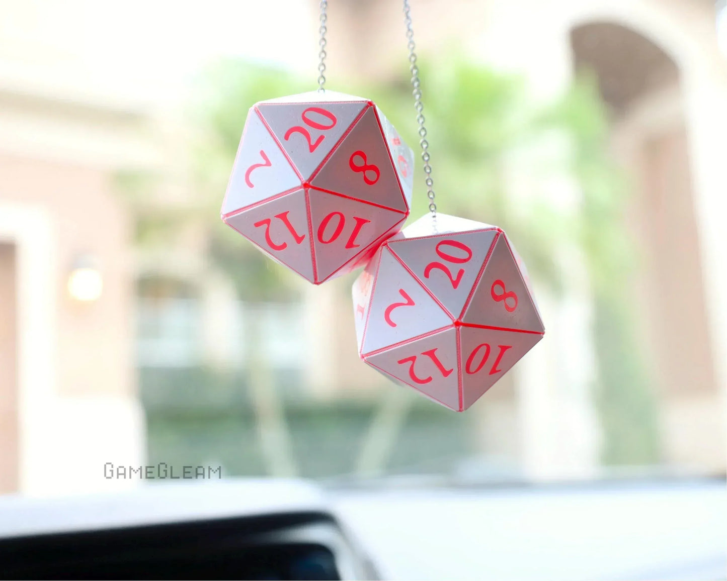 Handmade pink and white twenty-sided dice charms hanging from a car rearview mirror