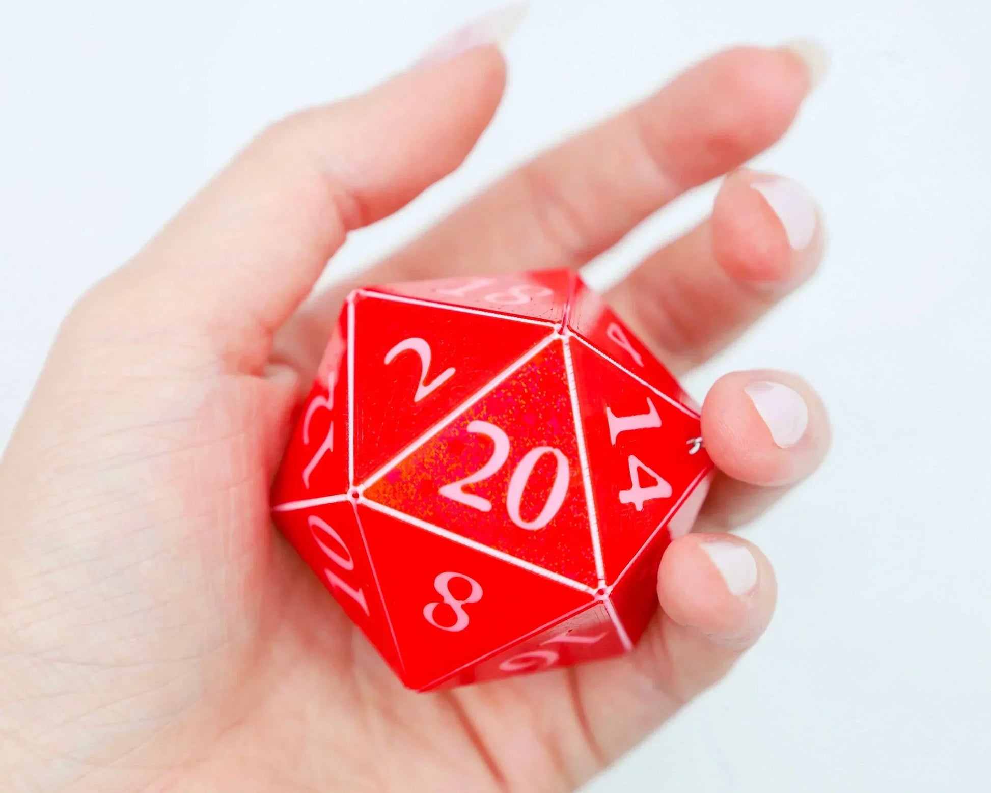 Hand holding large red twenty-sided polyhedral dice for tabletop games and RPG accessories