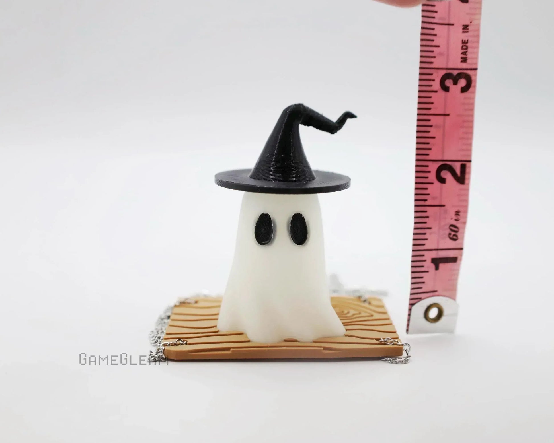Handmade ghost figurine with black witch hat, sitting on wood-pattern base, measured by tape