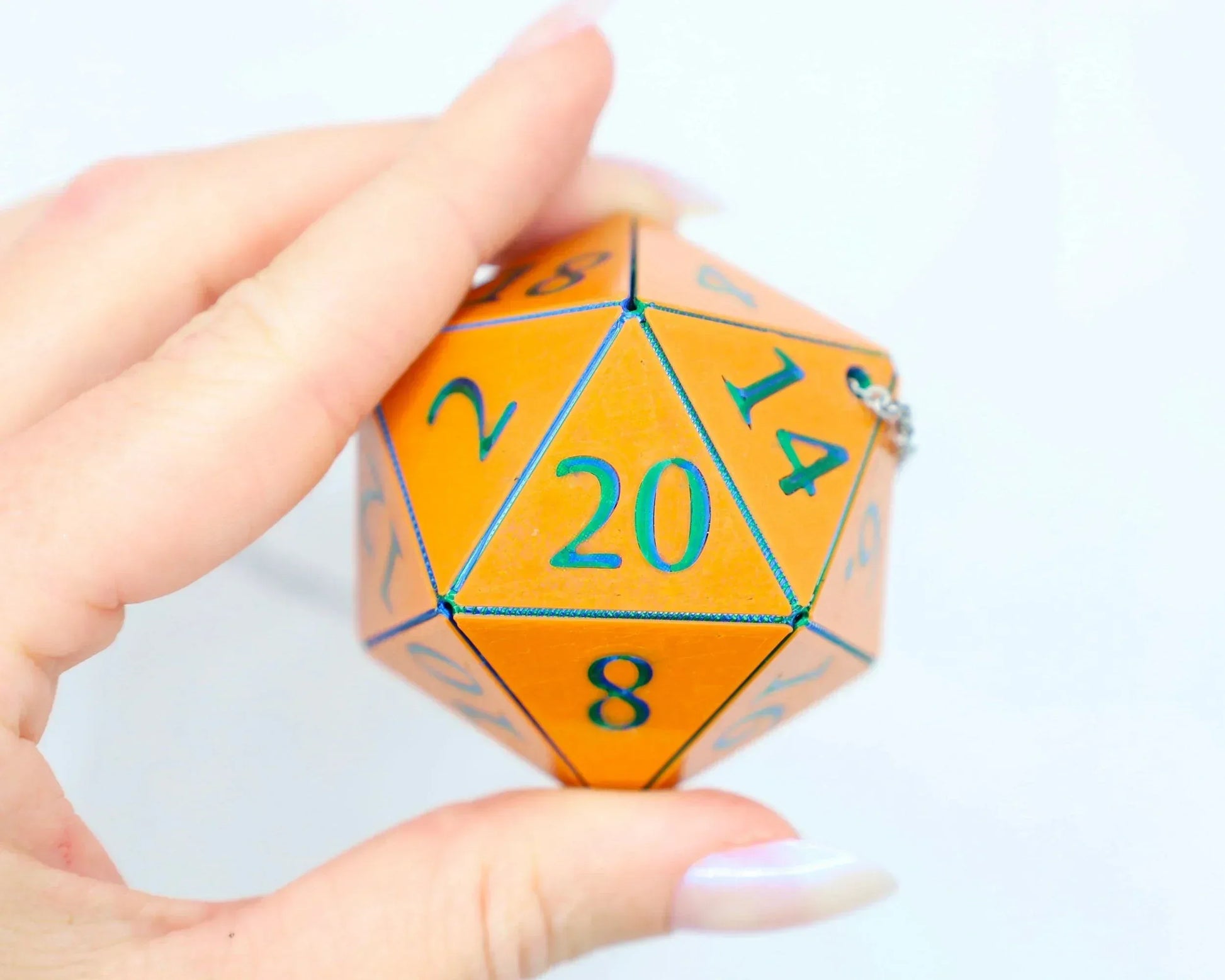 Hand holding an orange 20-sided dice car charm with blue numbers, gamer gift accessory