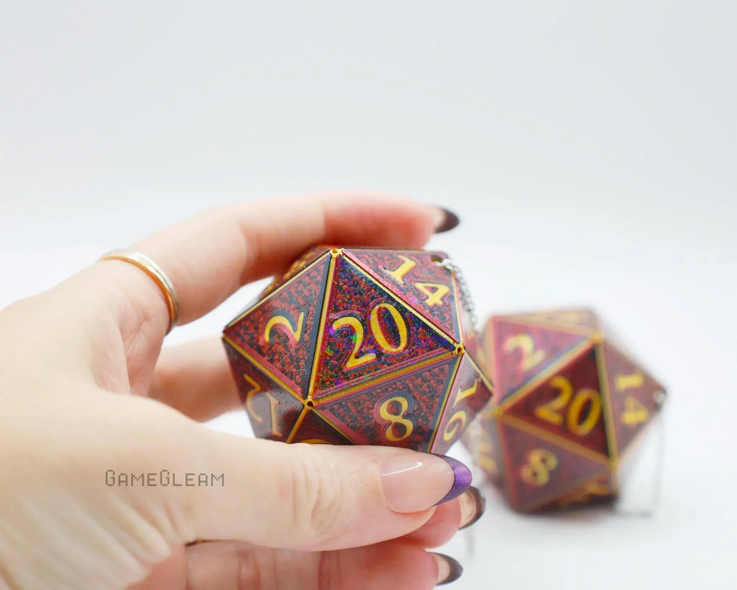 Hand holding a holographic red twenty-sided dice car charm with yellow numbers