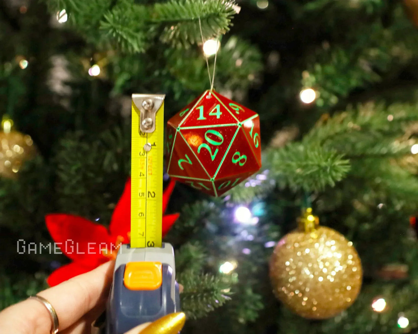 Red twenty-sided dice ornament with green numbers hanging on Christmas tree, measured by tape.