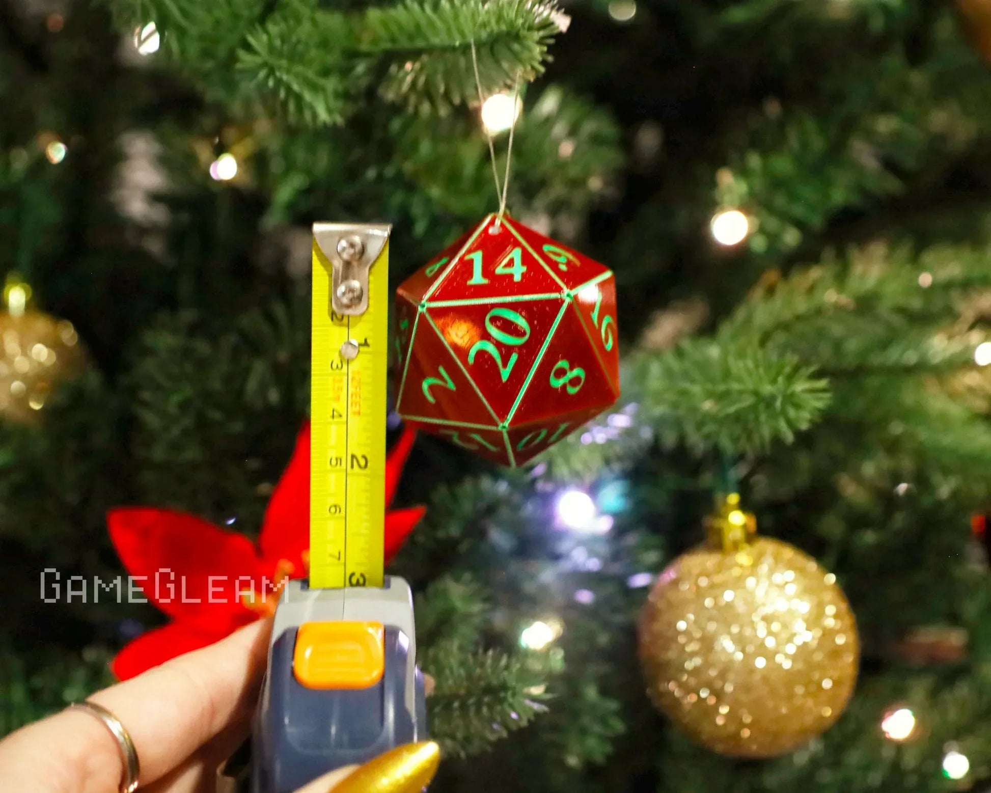 Red twenty-sided dice ornament with green numbers hanging on Christmas tree, measured by tape.