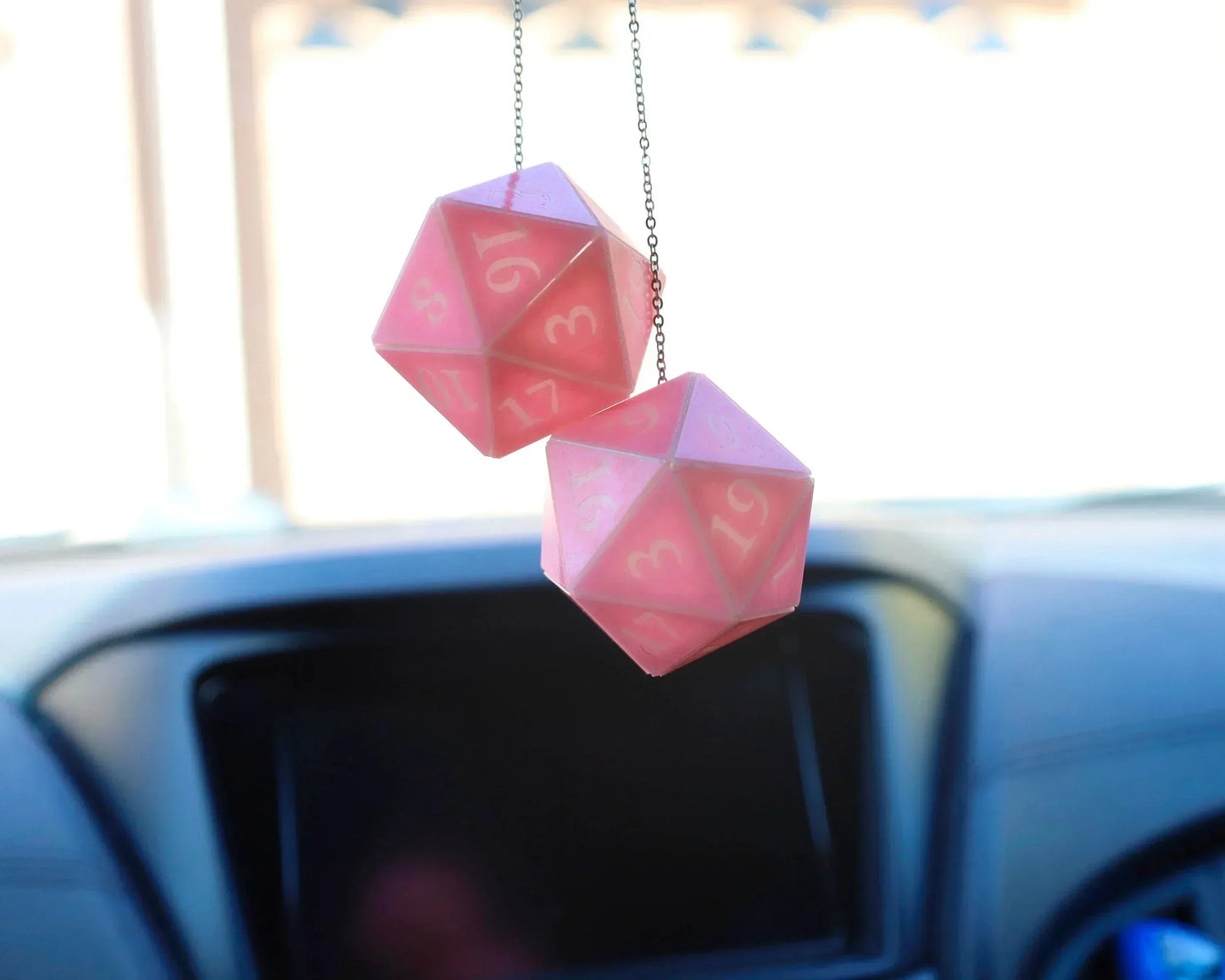 Pink 20-sided dice car charm hanging from rearview mirror in a car interior