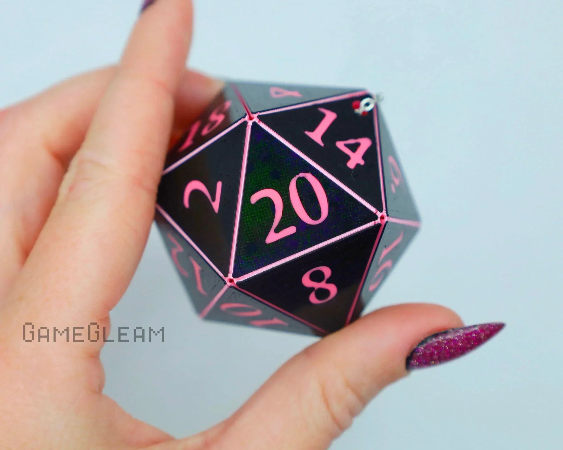 Hand holding a black 20-sided dice with pink numbers, ideal for tabletop RPG gaming.