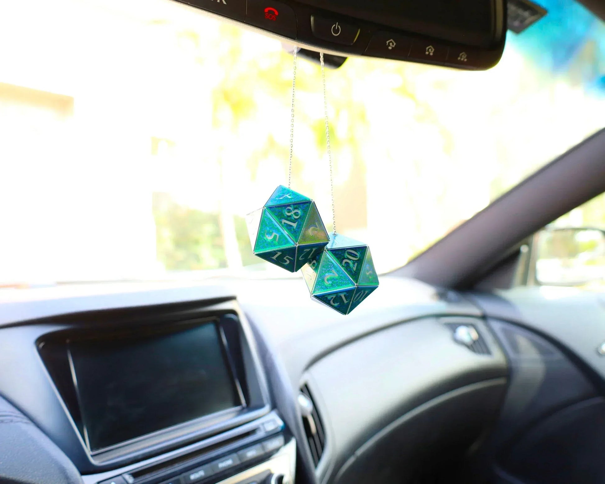 Holographic teal twenty-sided dice car charm hanging from rearview mirror in a vehicle.