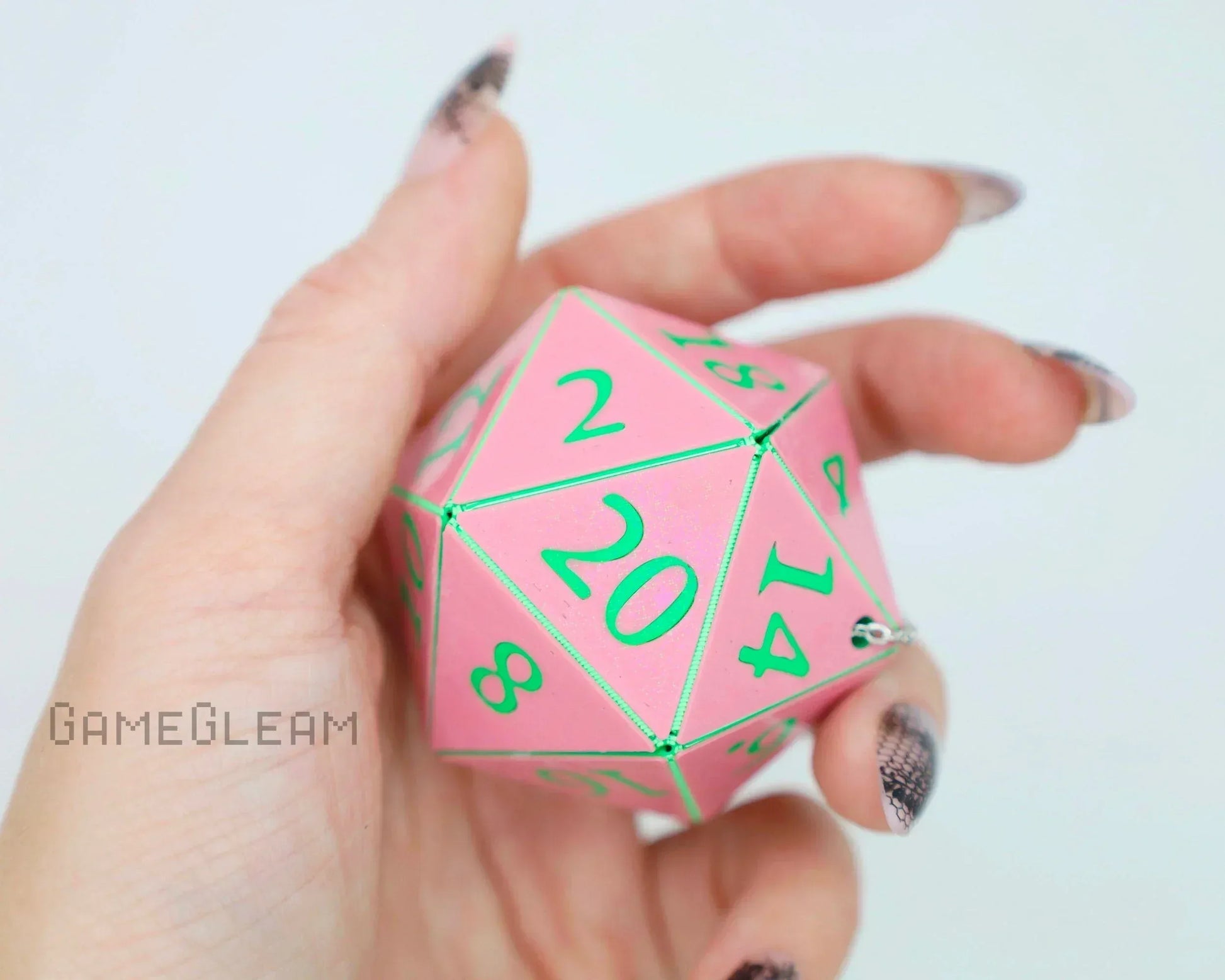 Hand holding large pink 20-sided dice with green numbers, perfect for tabletop gaming accessory.