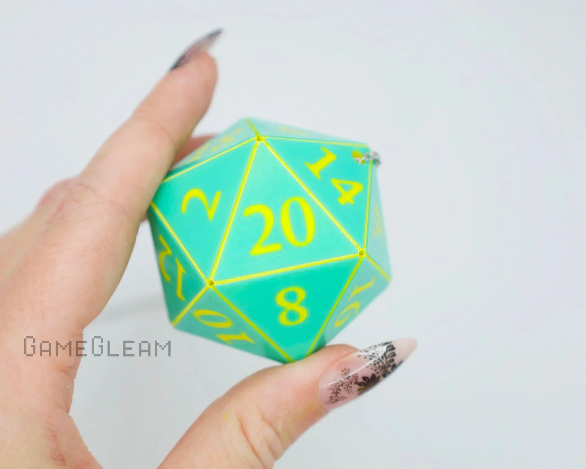 Hand holding a teal twenty-sided dice with yellow numbers, used as a car accessory charm.