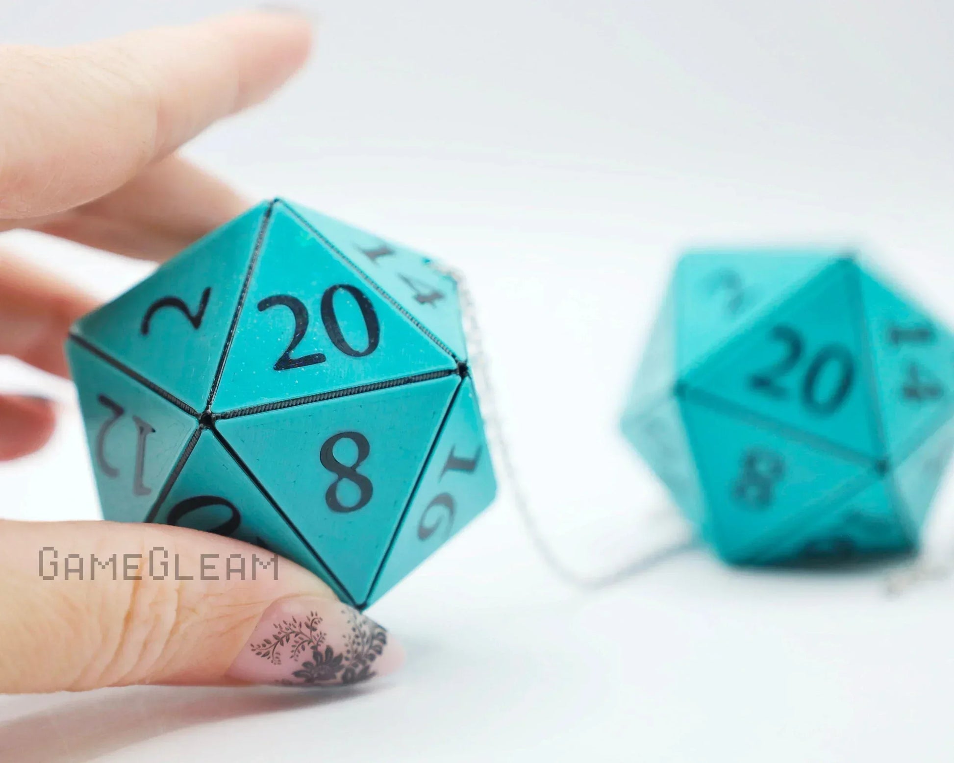 Hand holding teal 20-sided dice car charm with chain for tabletop gaming enthusiasts