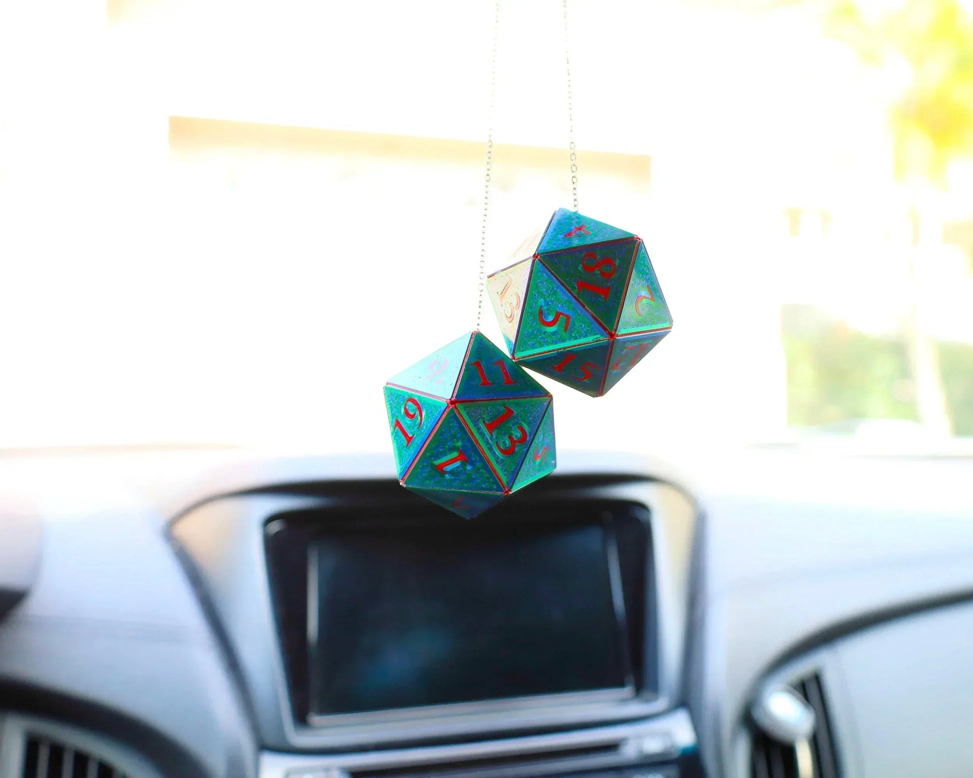 Holographic twenty-sided dice car charms hanging from a rearview mirror inside a car.