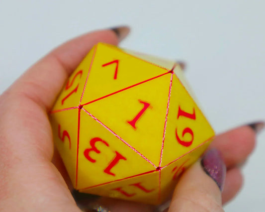 Hand holding a yellow twenty-sided polyhedral dice with red numbers, gamer accessory