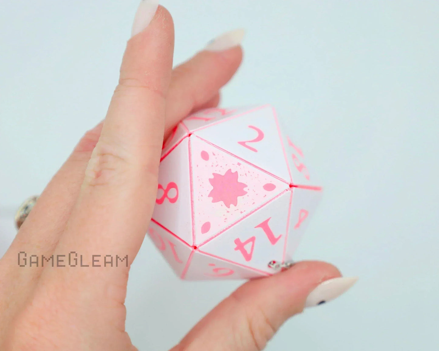 Hand holding a pink and white 20-sided polyhedral hanging dice charm for tabletop gaming or car decor