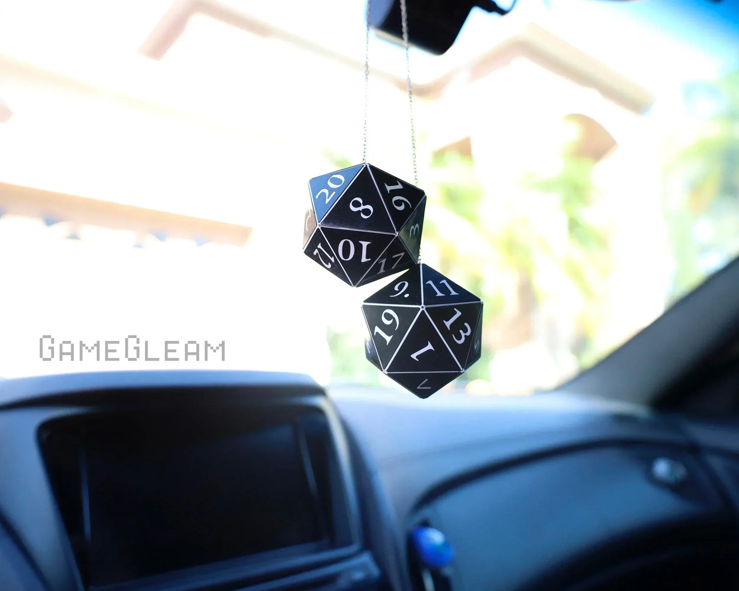 Black 20-sided dice car charm hanging from rearview mirror in bright car interior.
