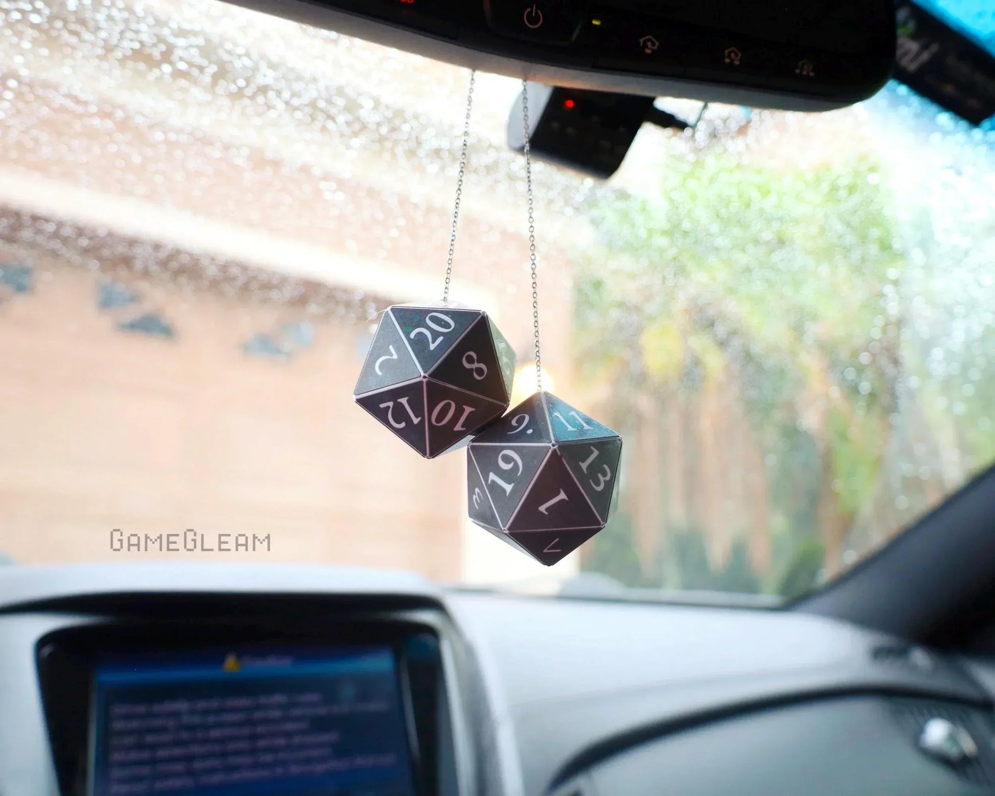 Hanging black twenty-sided dice car charms with white numbers, photographed in a vehicle.