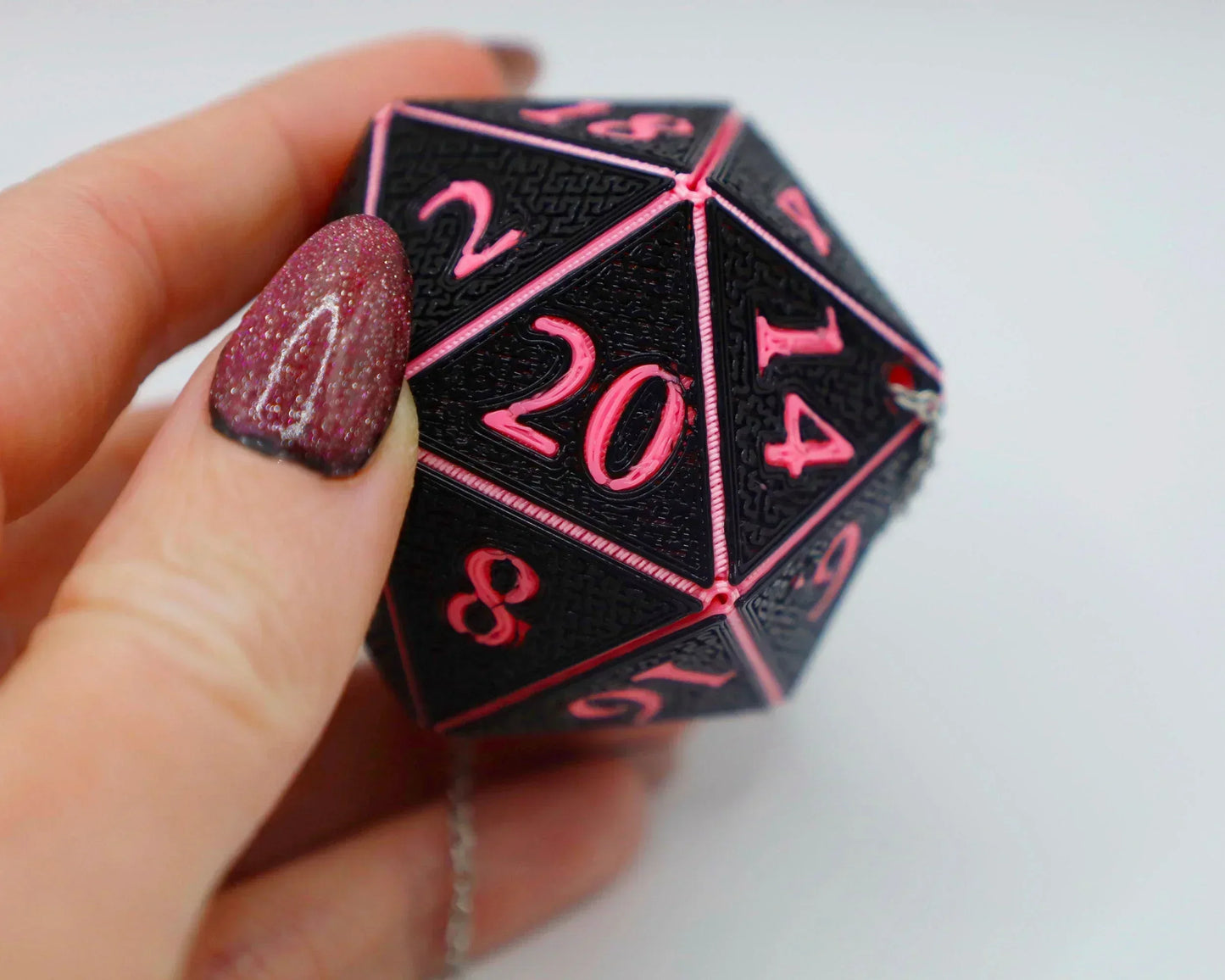 Hand holding a large black and pink 20-sided dice charm with visible chain for car accessory.
