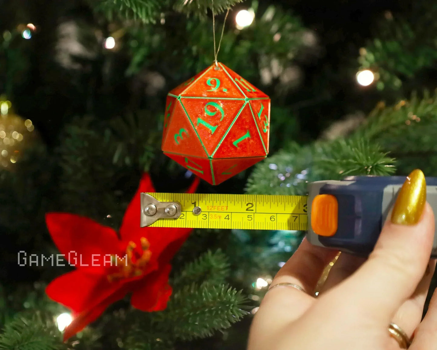 Red twenty-sided dice ornament hanging on Christmas tree with tape measure showing size