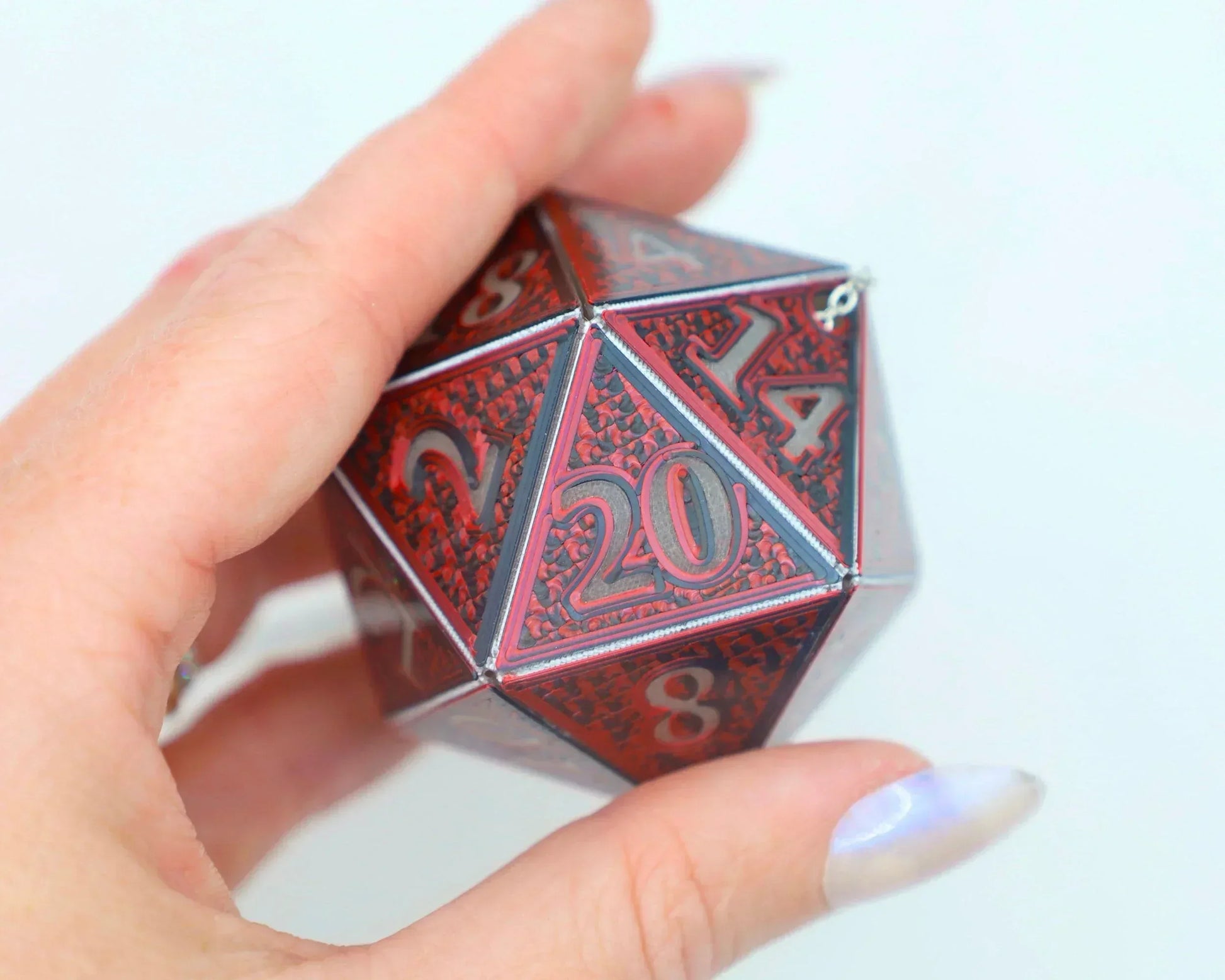 Hand holding large red holographic 20-sided gaming dice with engraved numbers