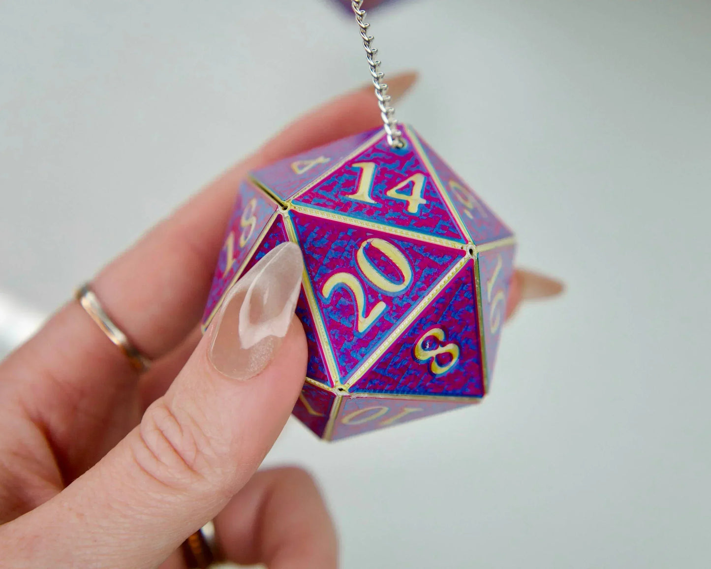 Hand holding a holographic purple and blue 20-sided dice car charm for RPG fans