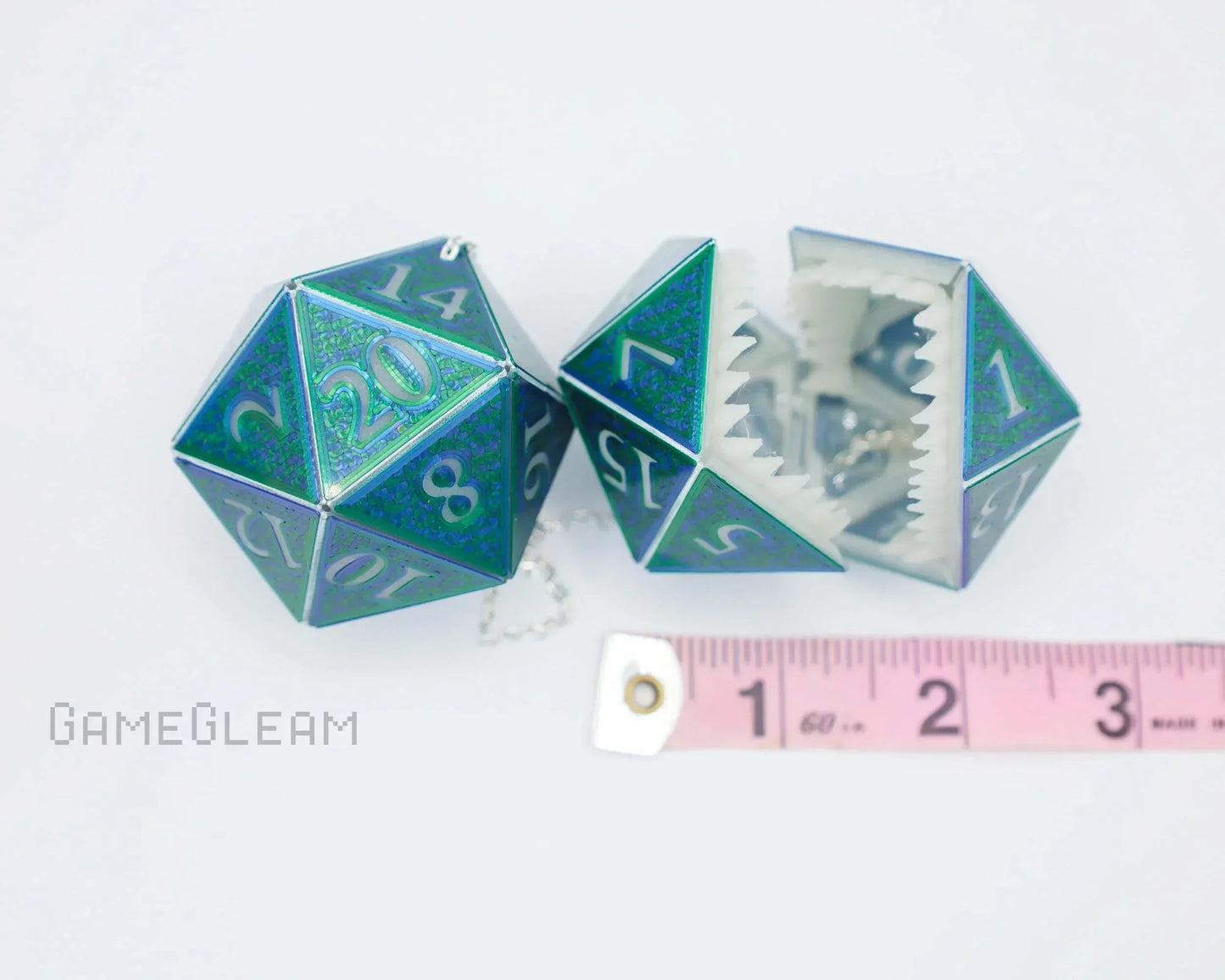 Holographic green and blue twenty-sided dice charms with teeth, next to a pink tape measure.