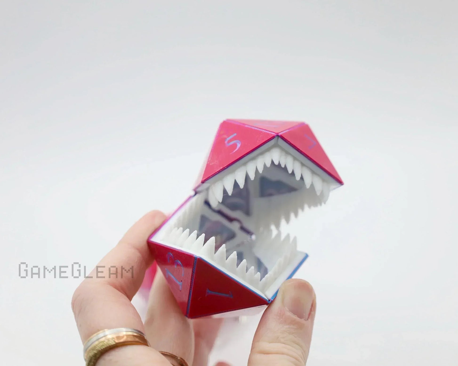 Hand holding red polyhedral dice charm with sharp teeth, unique gamer gift accessory