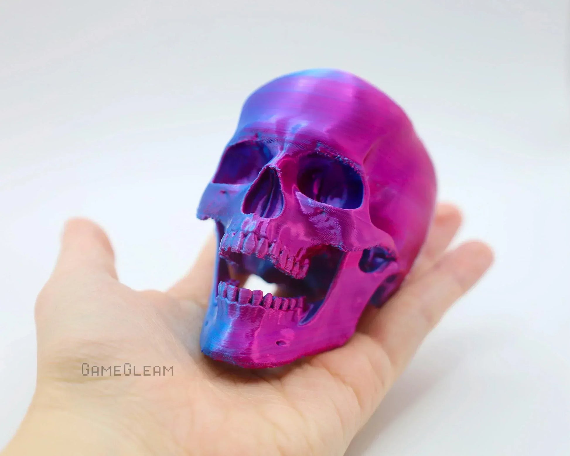 Hand holding iridescent purple and blue skull figurine, handmade gamer decor