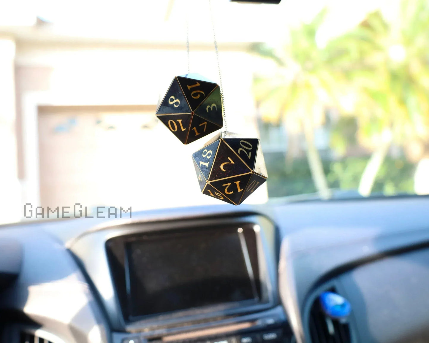 Black and gold 20-sided dice car charm hanging from rearview mirror in a car interior