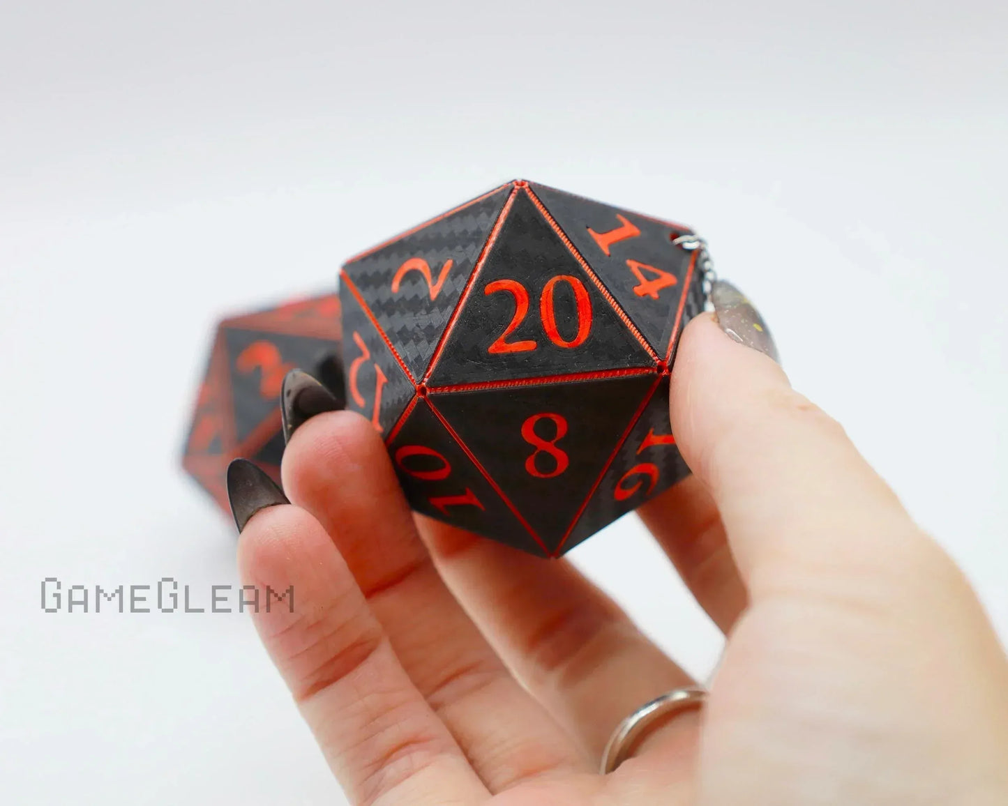 Hand holding a large black 20-sided dice with red numbers, carbon fiber texture, on keychain