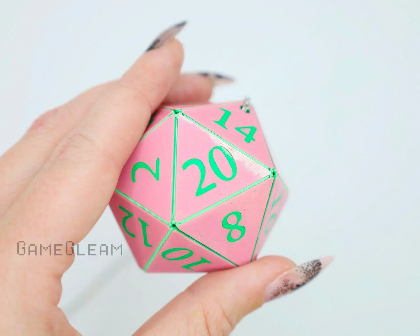 Hand holding a pink twenty-sided dice with green numbers, close-up tabletop accessory.