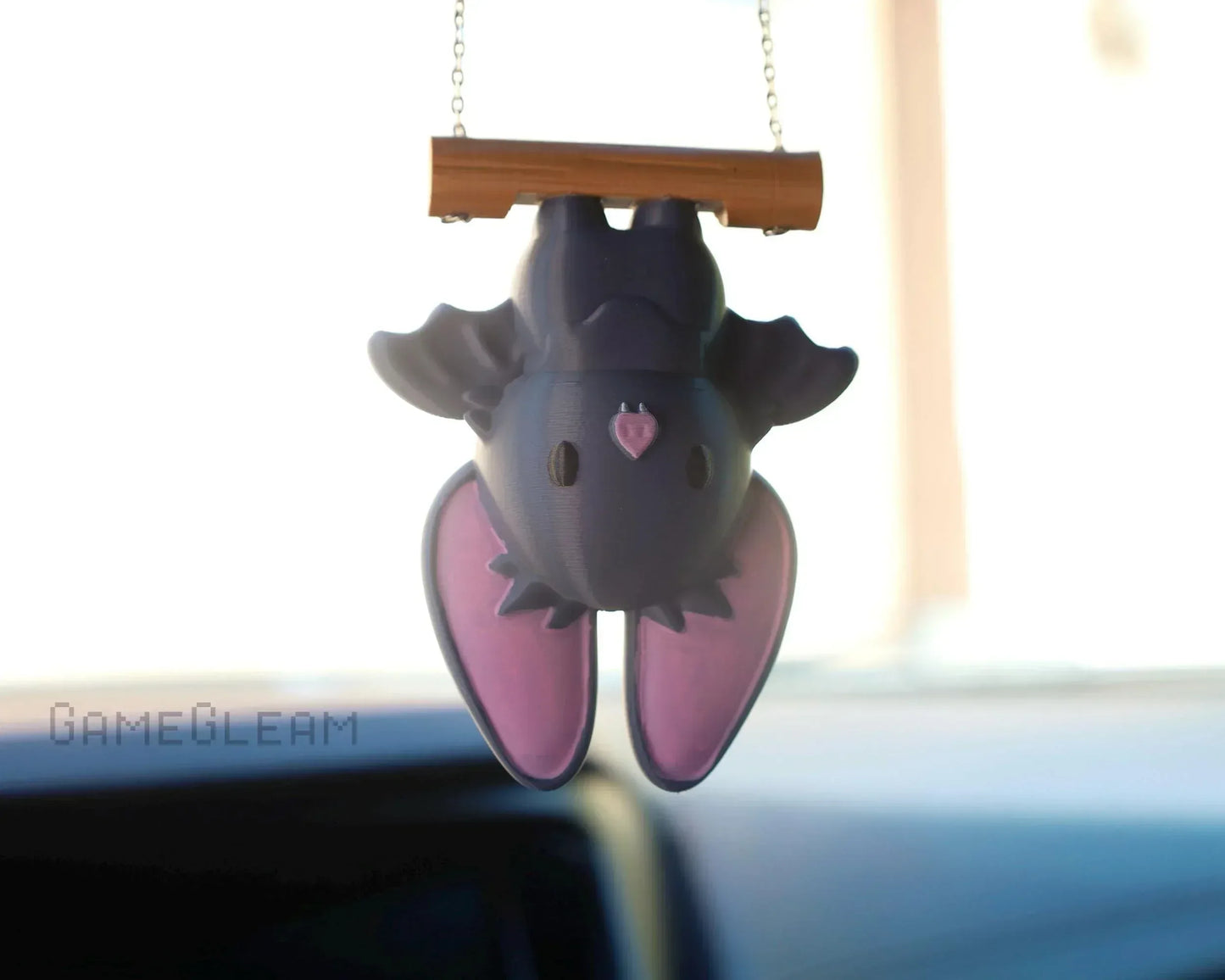 Cute handmade bat car charm with purple wings, hanging upside down from a wooden bar