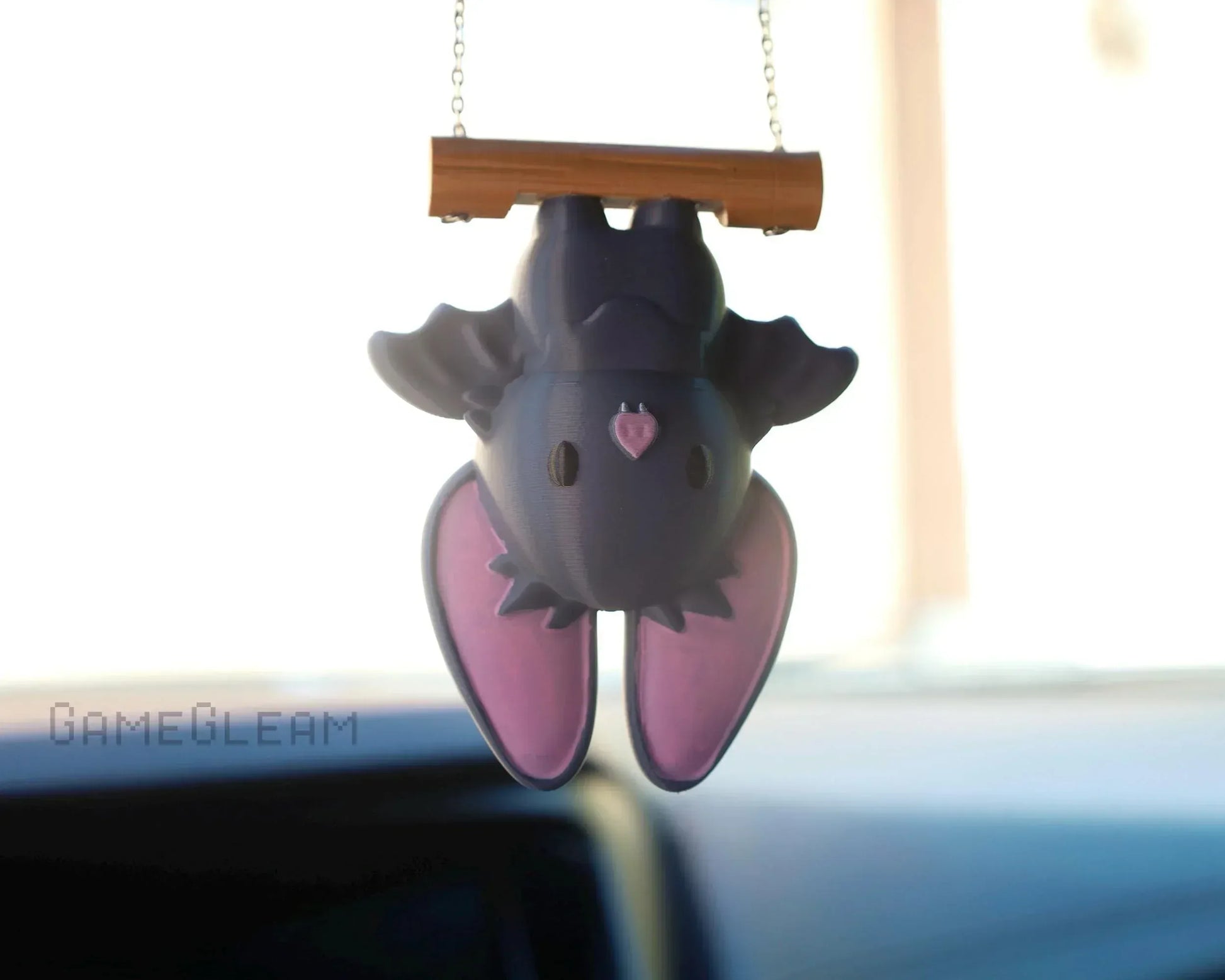 Cute handmade bat car charm with purple wings, hanging upside down from a wooden bar