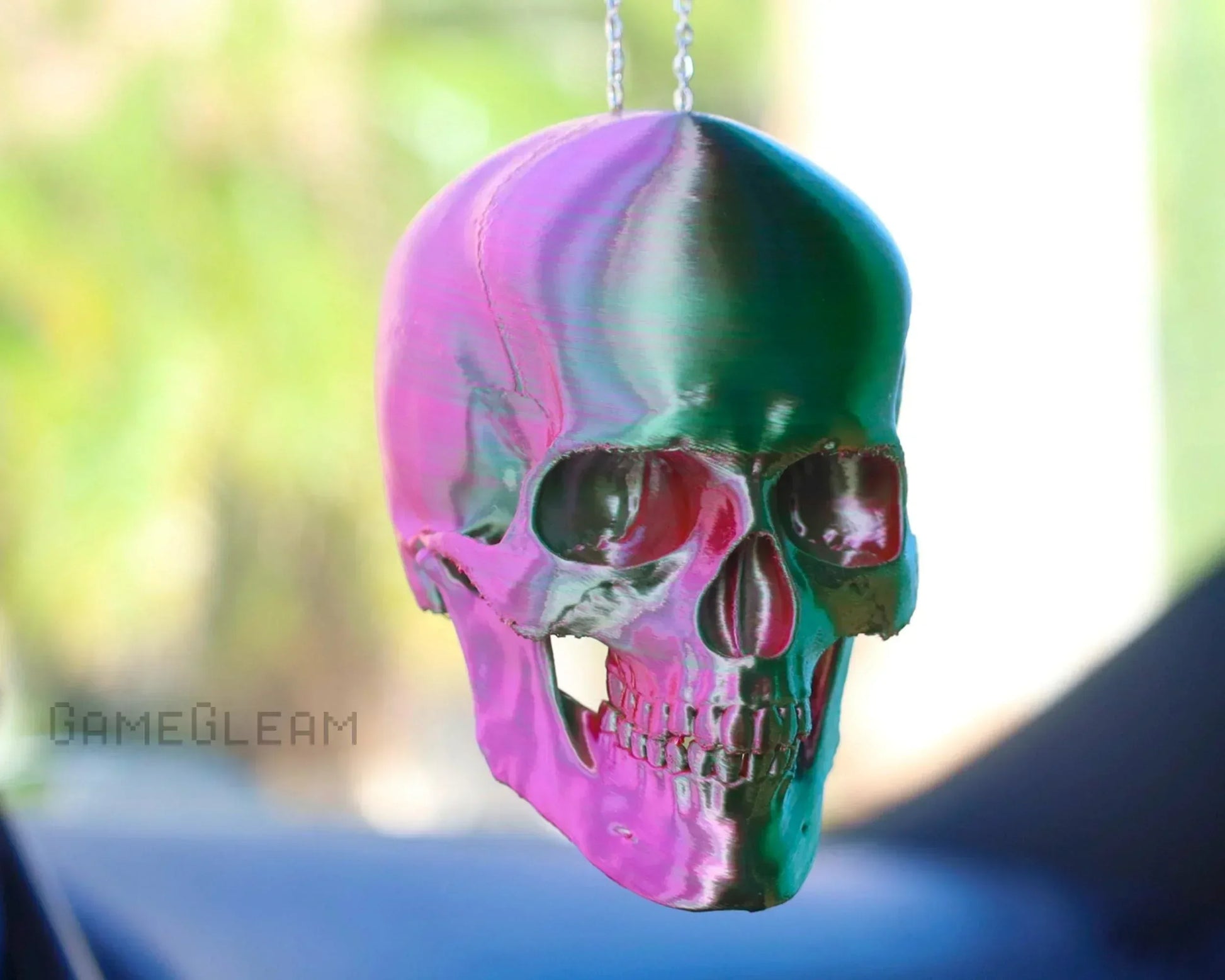 Holographic pink and green skull charm hanging from car rearview mirror, vibrant decor accessory