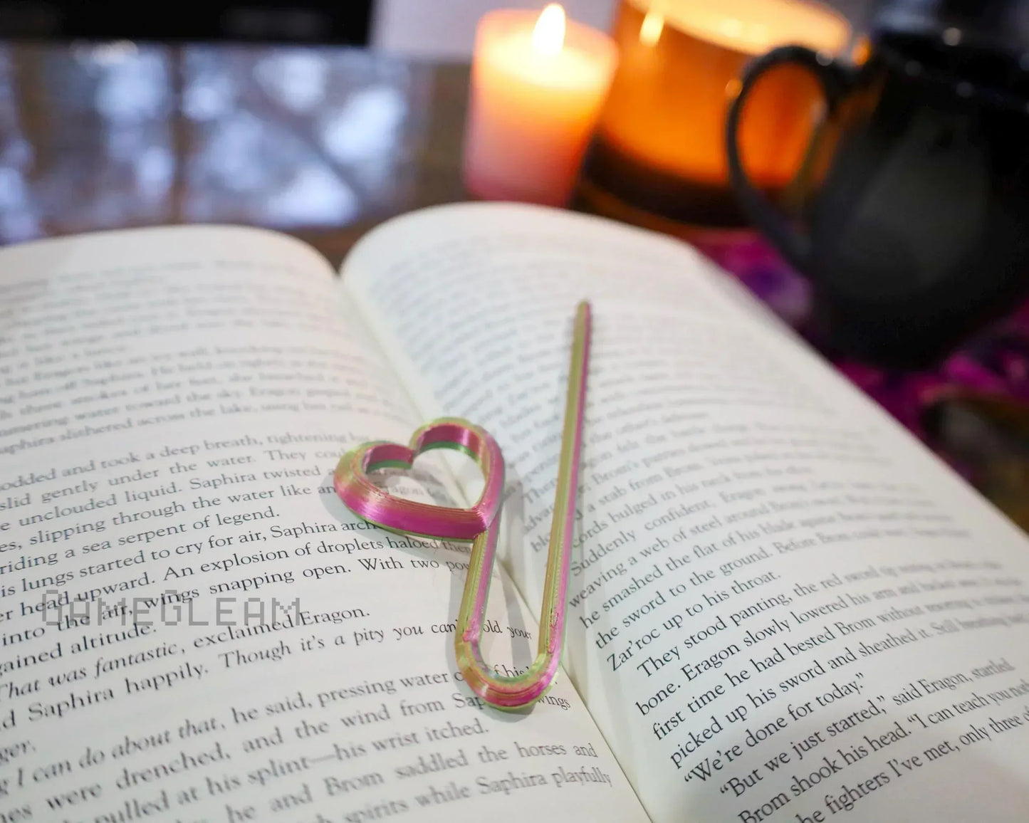 Heart-shaped metal bookmark on open book with candles and coffee mug in background