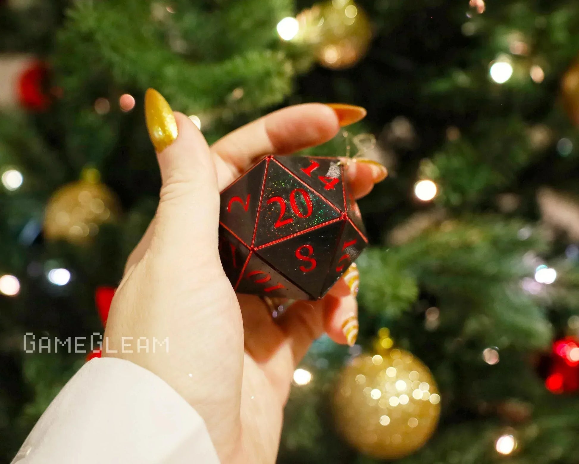 Hand holding black and red twenty-sided dice ornament near a decorated Christmas tree.
