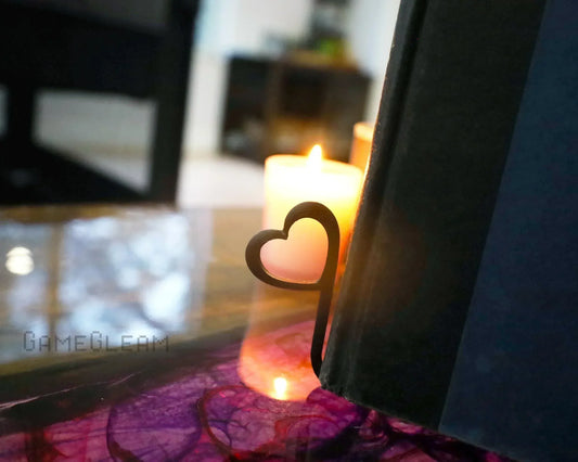 Metal heart-shaped bookmark in book, lit candle in background on purple table