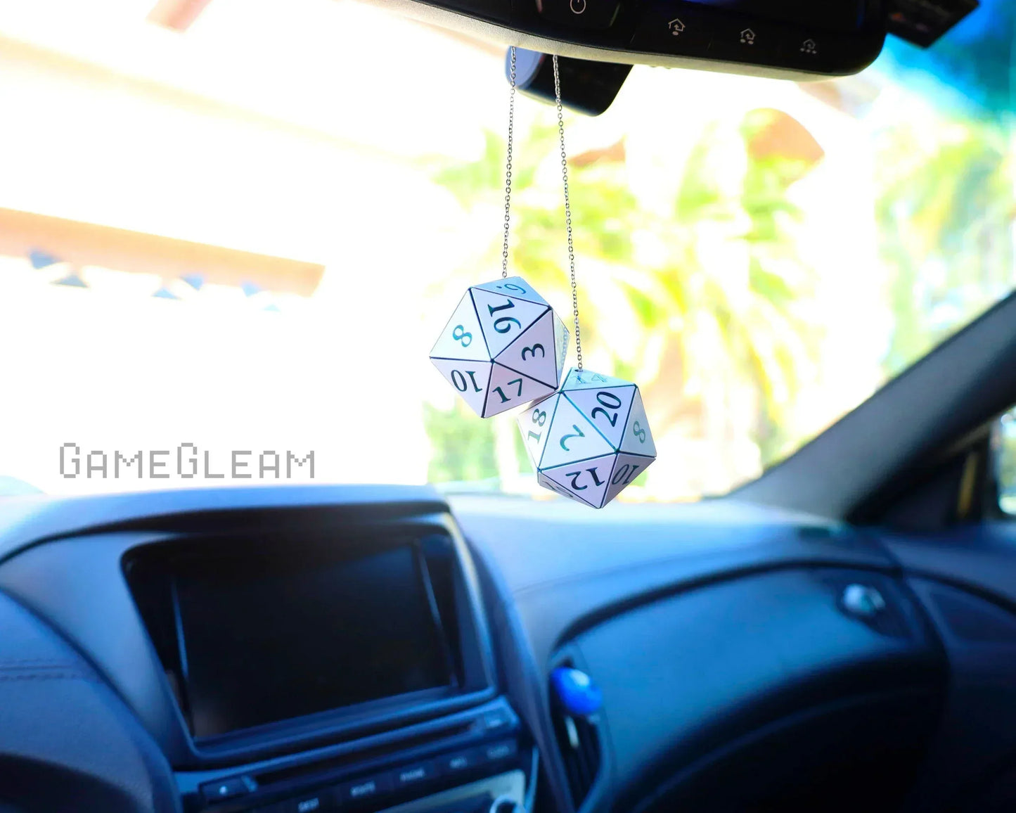 White twenty-sided dice charms hanging from a car mirror in a modern car interior.