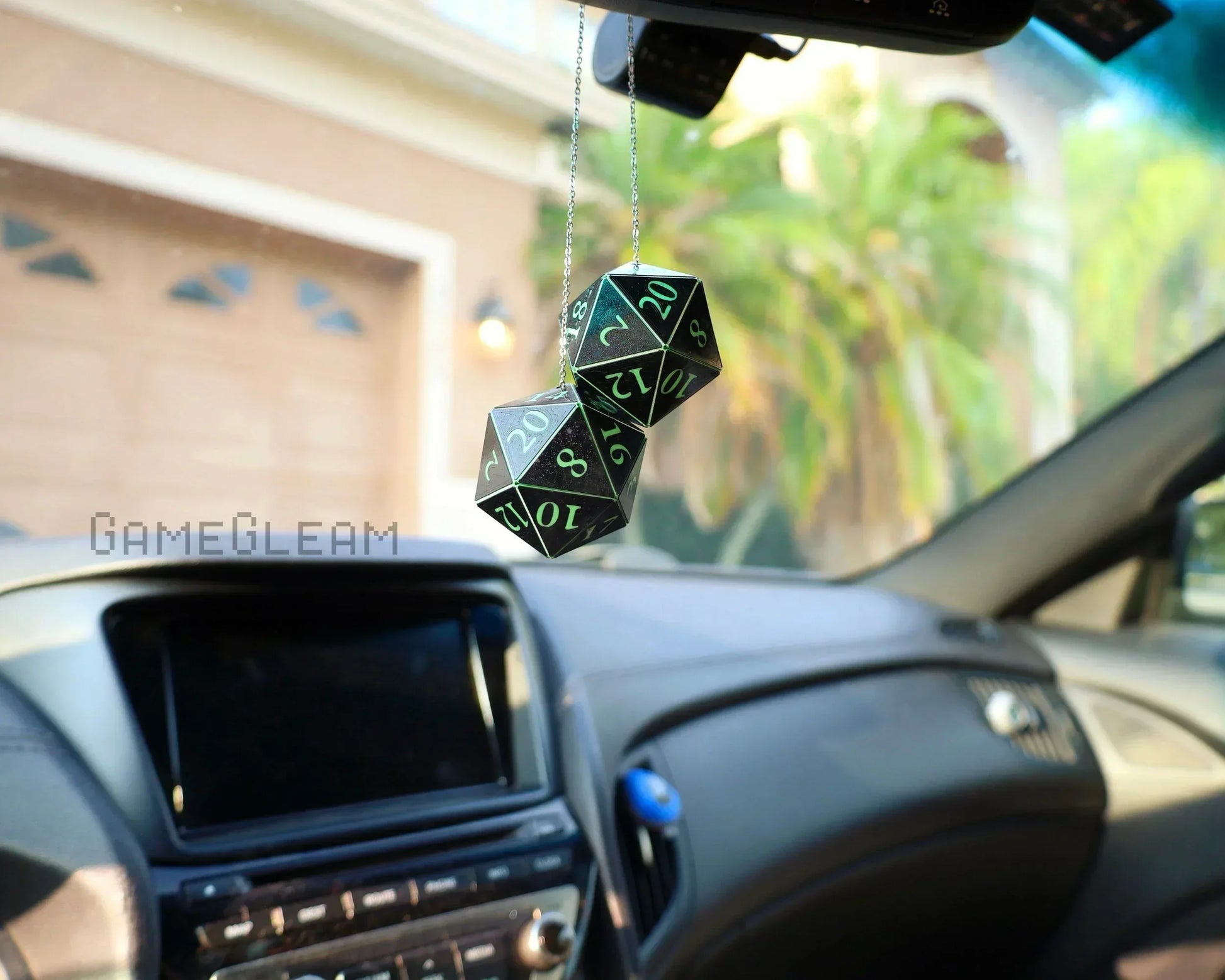 Black and green twenty-sided dice car charm hanging from rearview mirror inside a vehicle