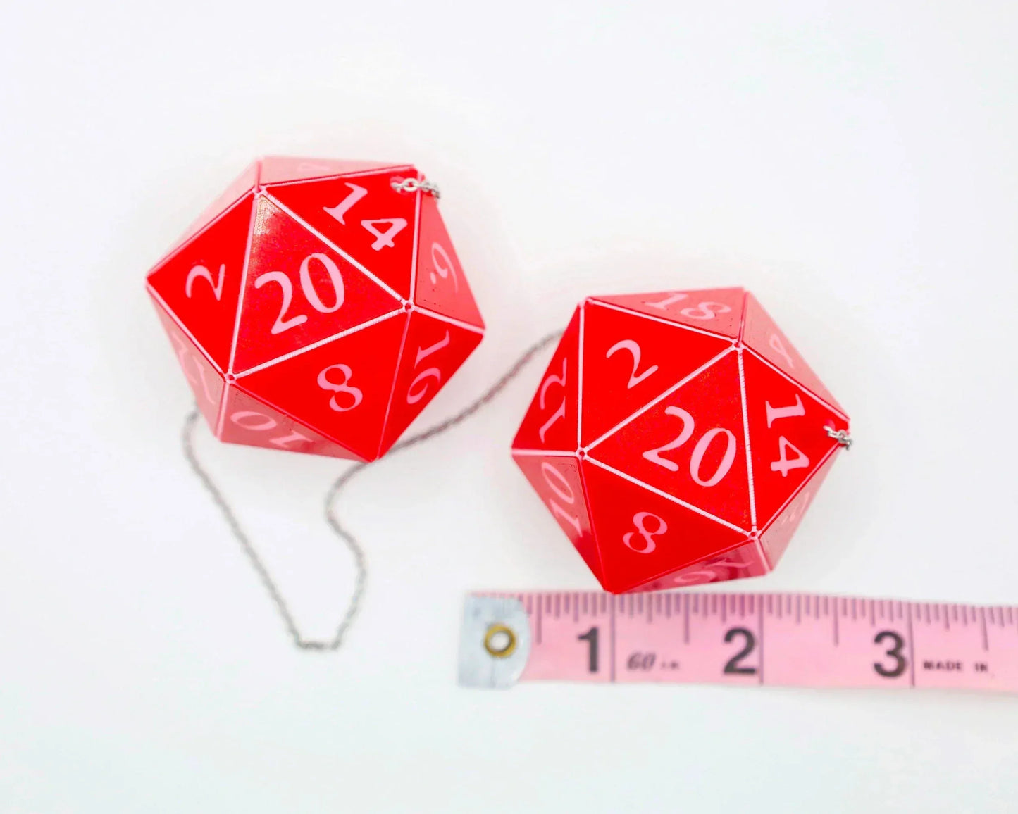 Red twenty-sided dice car charms with white numbers and chain next to a measuring tape