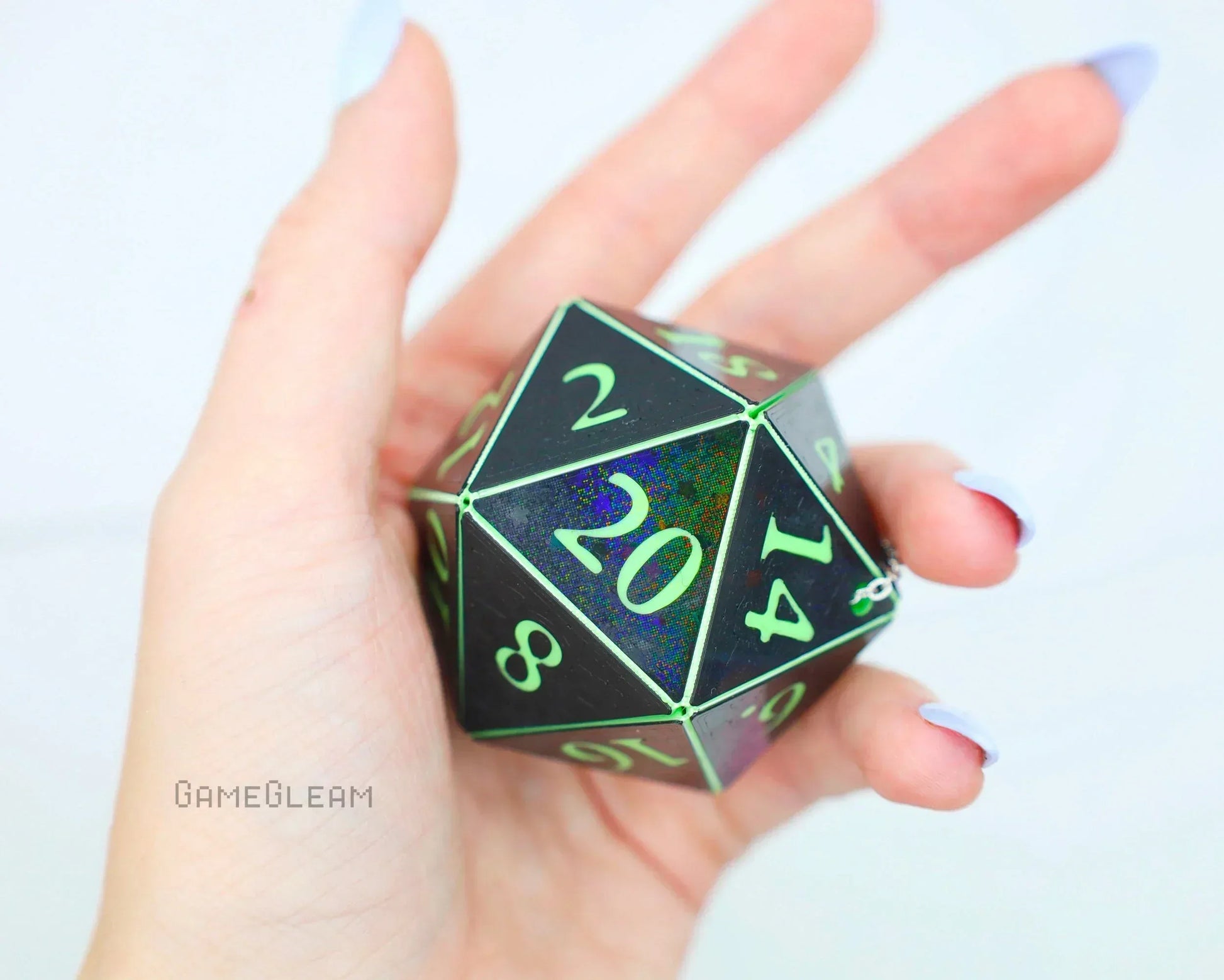 Hand holding large holographic black 20-sided dice with green numbers, gamer accessory